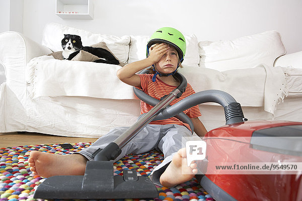 Exhausted boy in living room with cat and vacuum cleaner