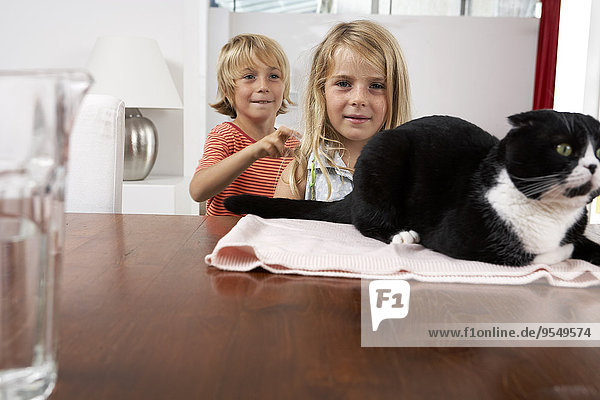 Brother and sister with cat on dining table