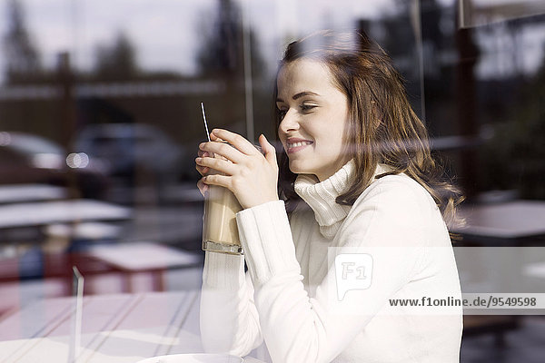 Lächelnde junge Frau mit Latte Macchiato sitzend in einem Cafe und schauend