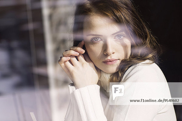 Porträt einer jungen Frau  die durch die Fensterscheibe eines Cafés schaut.