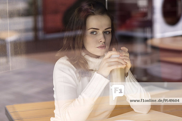 Porträt einer jungen Frau mit Latte Macchiato in einem Café mit Blick durch die Fensterscheibe