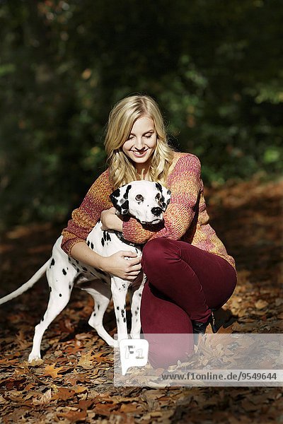 Smiling blond woman with Dalmatian in autumnal forest