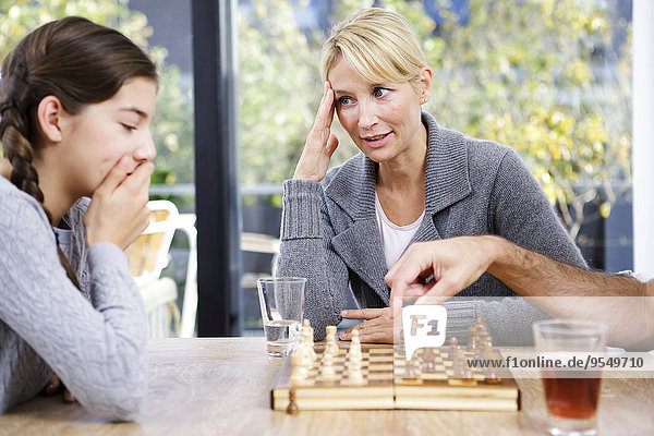 Vater und Tochter spielen zu Hause Schach  Mutter schaut zu.
