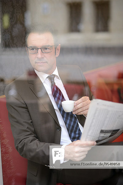 Ein Geschäftsmann sitzt in einem Café mit einer Zeitung und schaut sich etwas an.