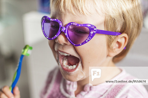 Porträt eines kleinen Mädchens mit Sonnenbrille beim Zähneputzen