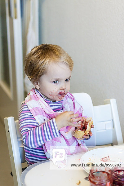 Kleines Mädchen mit Lätzchen versucht  Marmeladenbrötchen zu essen.