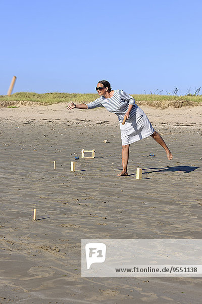 Frau spielt Kubb am Strand