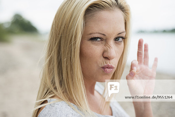 Portrait of young blond woman pouting mouth and showing ok sign
