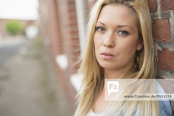 Portrait of young serious looking woman leaning against brick wall