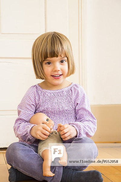 Porträt eines lächelnden kleinen Mädchens,  das mit einer Puppe spielt.