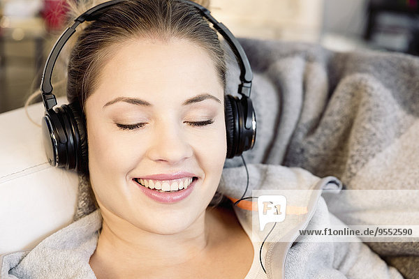Entspannte junge Frau zu Hause mit Kopfhörer