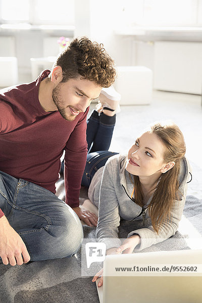 Smiling young couple with laptop on floor