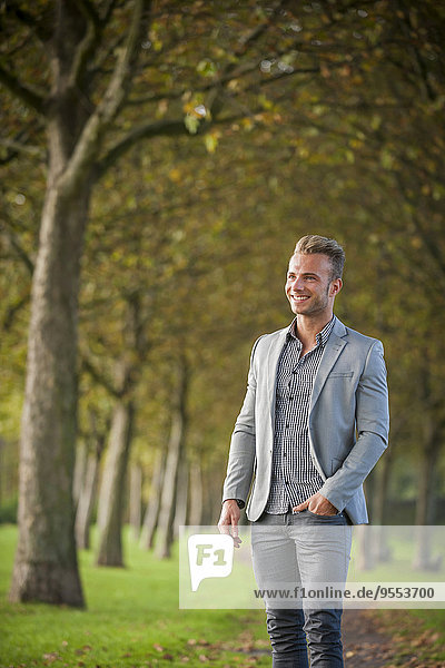 Lächelnder junger Geschäftsmann steht im Park