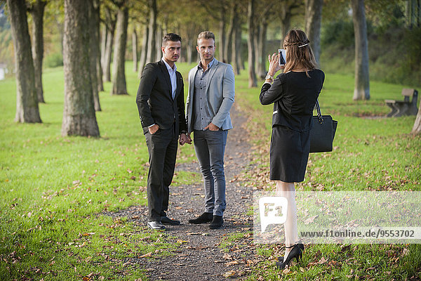 Young businesswoman photographing business partners with her smartphone in a park