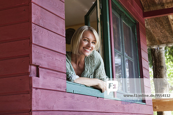Lächelnde reife Frau schaut aus dem Fenster des Sommerhauses