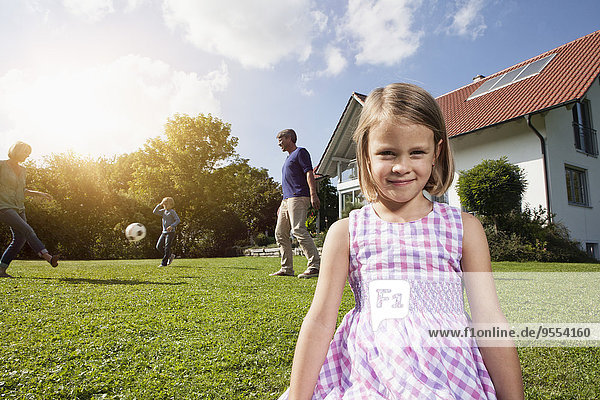 Smiling girl with family playing soccer in garden