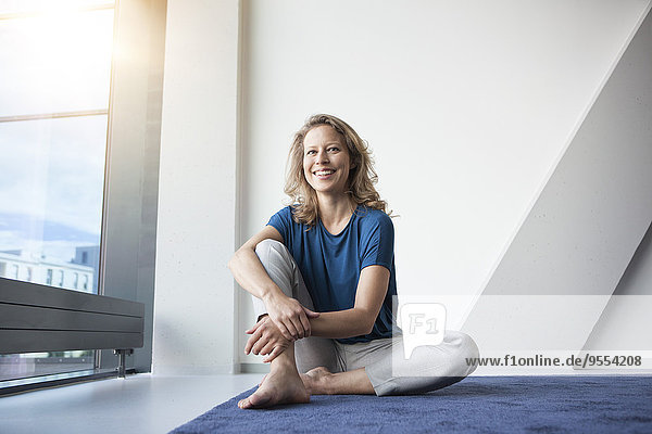 Portrait of smiling mature woman sitting on the floor at her apartment