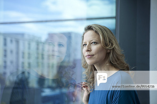 Portrait of mature woman looking through window at her apartment