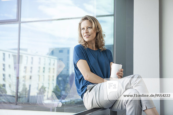 Smiling mature woman looking through window at her apartment
