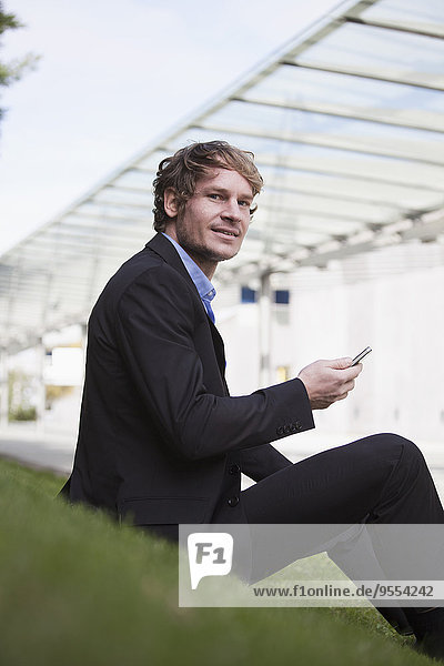 Businessman sitting on a meadow with smartphone