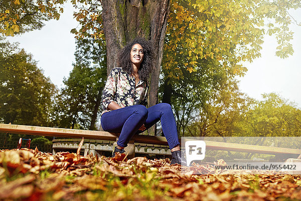 Porträt einer lächelnden jungen Frau mit Afro auf einer Parkbank sitzend