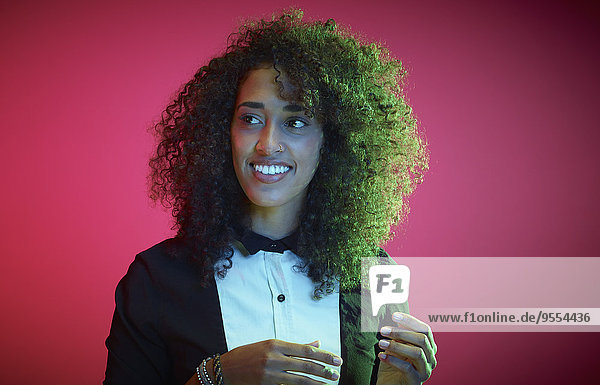Porträt einer lächelnden jungen Frau mit Afro vor rotem Hintergrund  die etwas beobachtet.