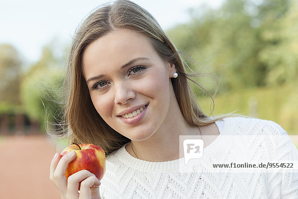 Porträt eines lächelnden blonden Mädchens  das einen Apfel isst.