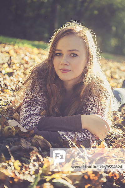 Porträt eines jungen Mädchens  das auf dem Boden liegt und mit Herbstlaub bedeckt ist.