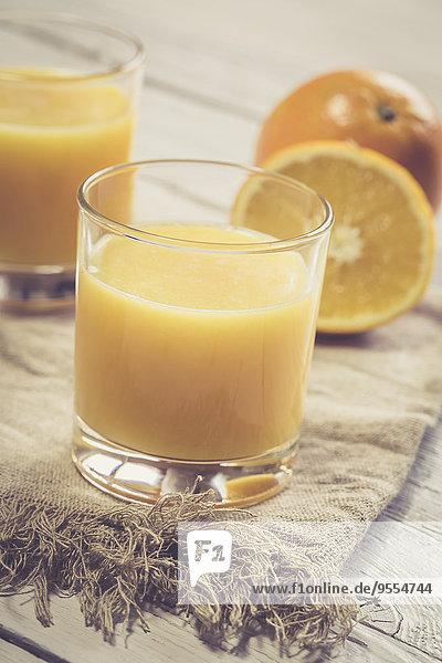 Zwei Gläser frisch gepresster Orangensaft und Orangen auf Tuch und Holz