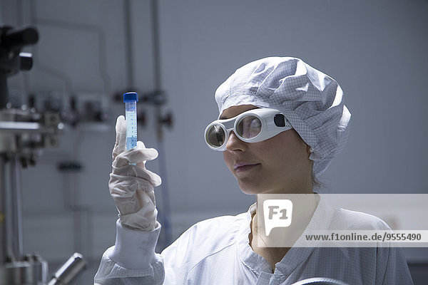 Young female technician with protective cap and safety glasses watching a tube in a labroratory