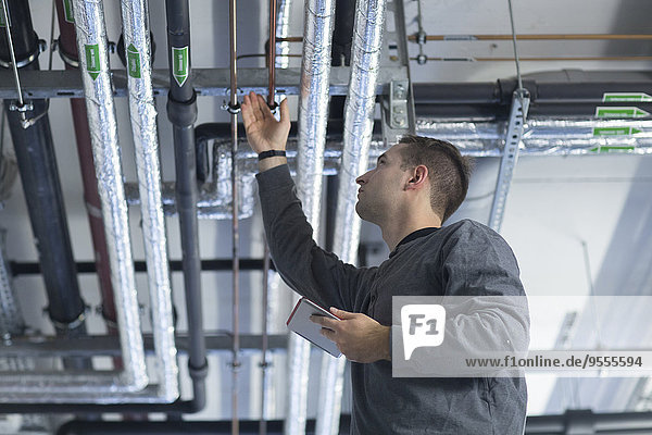 Young man with digital tablet in technical room checking pipe