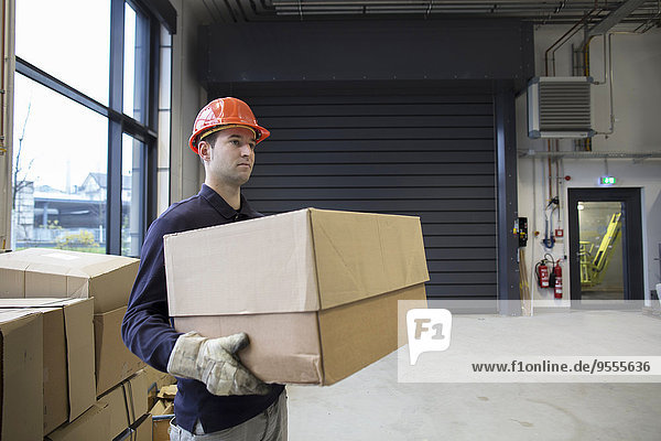 Young technician carrying cardboard box at an industrial hall