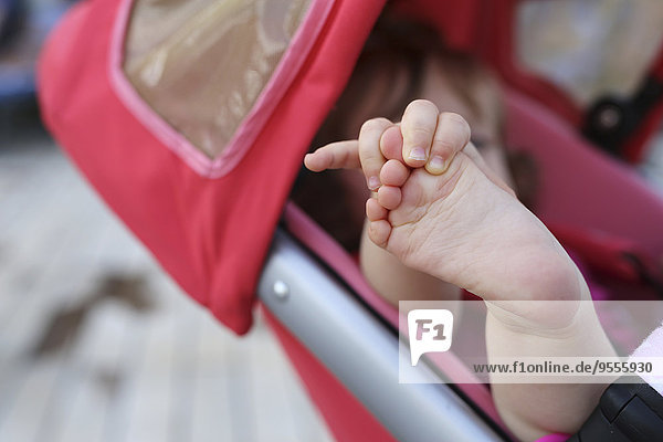 Kleines Mädchen im Kinderwagen beim Spielen mit dem Fuß