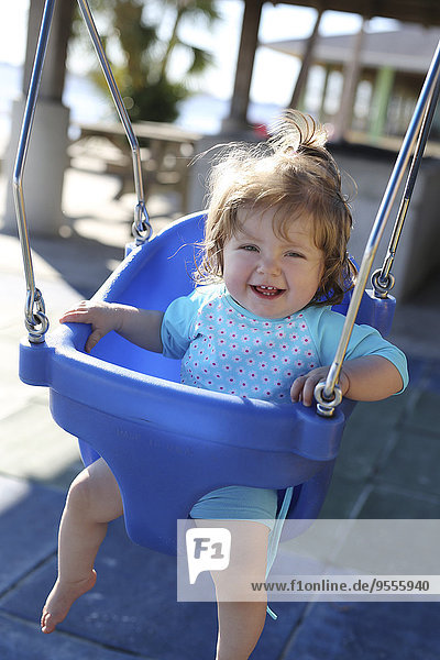 Lächelndes Mädchen auf blauer Babyschaukel sitzend
