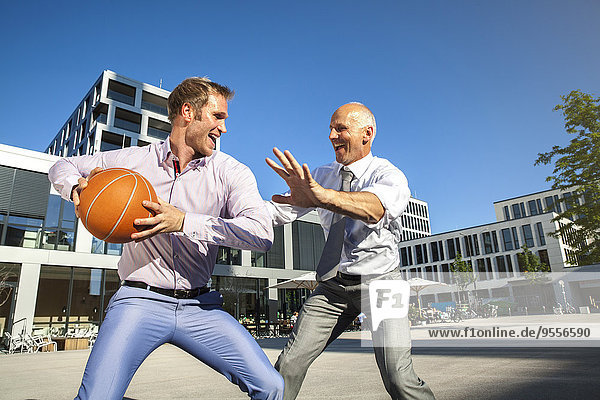 Two businessmen playing basketball outdoors