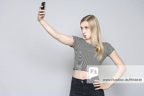 Porträt einer jungen Frau  die einen Selfie mit einem Smartphone nimmt.