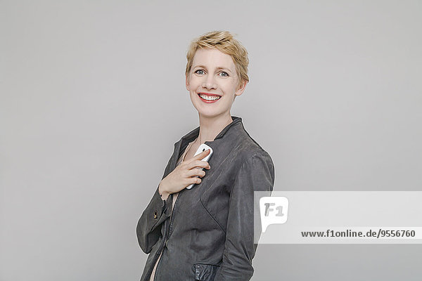 Portrait of smiling blond woman with smartphone in front of grey background
