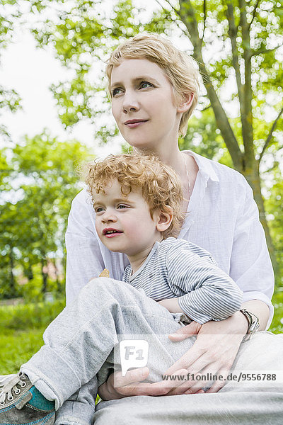 Mother and little son sitting together on a meadow watching something