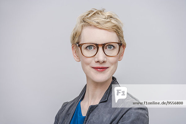 Porträt einer lächelnden blonden Frau mit Brille vor grauem Hintergrund