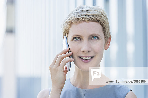 Porträt einer lächelnden blonden Frau beim Telefonieren mit dem Smartphone nach oben