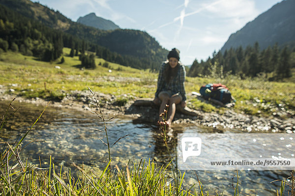 Austria  Tyrol  Tannheimer Tal  young female hiker relaxing at a brook