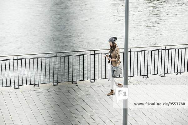 Junge Frau geht an der Promenade und orientiert sich mit einem digitalen Tablett.