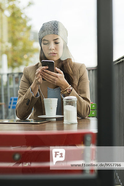 Junge Frau sitzt auf dem Bürgersteig Cafe mit Smartphone