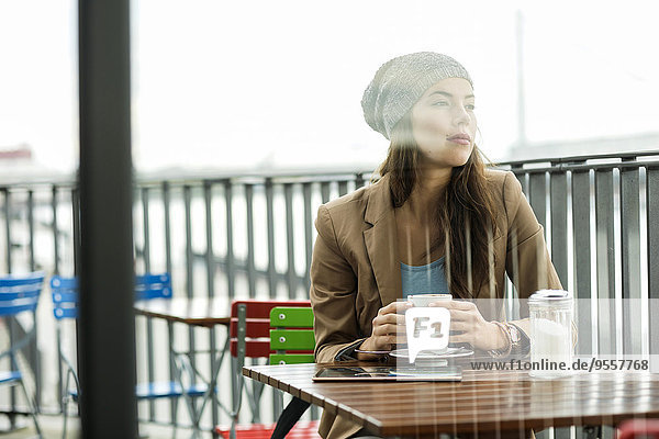 Tagträumende junge Frau sitzend im Straßencafé