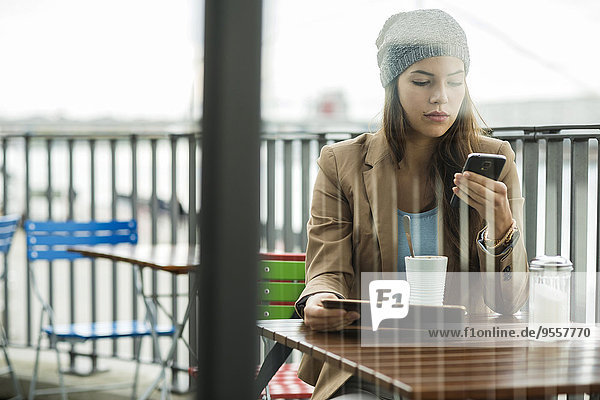 Junge Frau sitzt auf dem Bürgersteig Cafe halten digitale Tablette  während Sie mit dem Smartphone