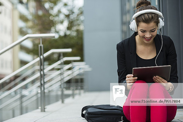 Junge Frau mit Kopfhörer auf der Treppe sitzend mit digitalem Tablett