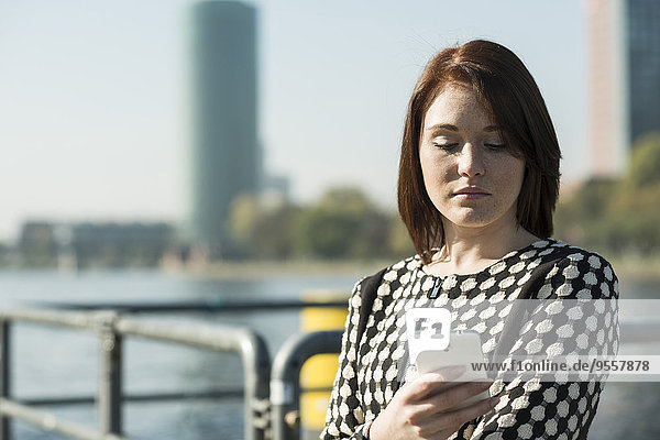 Deutschland  Frankfurt  junge Geschäftsfrau am Flussufer mit Handy