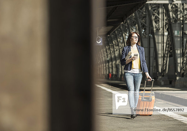 Junge Frau mit Handy und Gepäck am Bahnhof