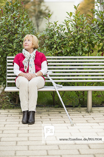 Seniorin mit Krücke auf einer Bank sitzend
