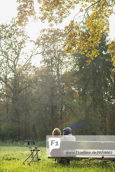 Seniorin und Enkelin auf einer Parkbank sitzend  Rückansicht